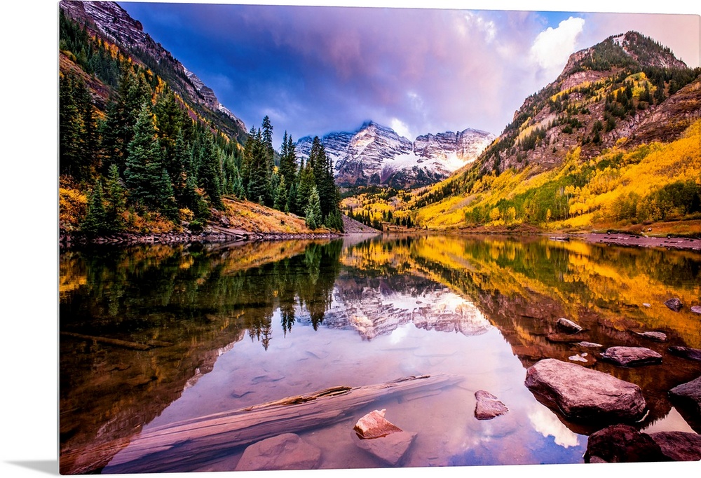 There is a warm hue to this photograph of mountainous terrain and thick foliage that reflect in still water below.