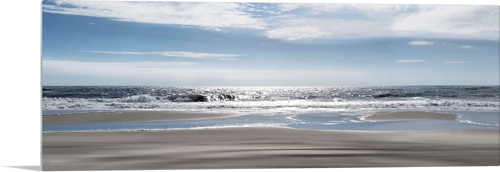 A panoramic photo illustrating a tranquil view of the beach as the sun shimmers on the sea.