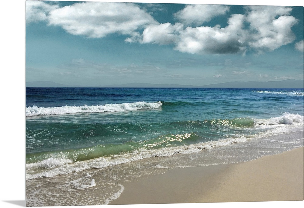 This serene photo shows rippling waves as they approach the beach with puffy white clouds in the background.