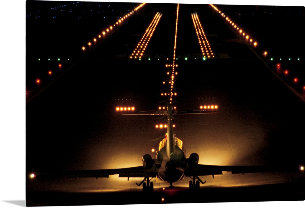 Giant photograph shows a small aircraft stationed at the end of a brightly lit airstrip at nighttime.