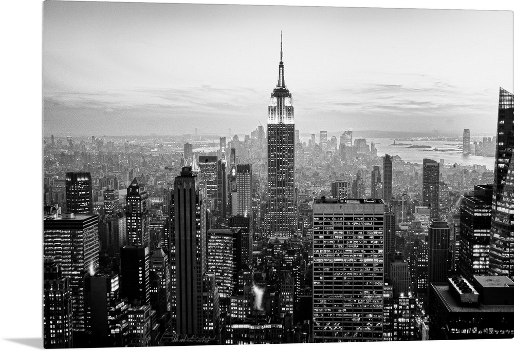 High angled photograph of city buildings at dusk.  The building windows are filled with light creating little rectangle pa...