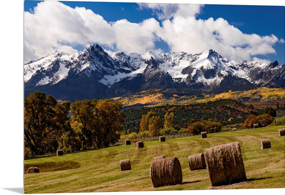 Grazing land at the foot of snow covered mountains and rustic autumn trees in a landscape photograph.