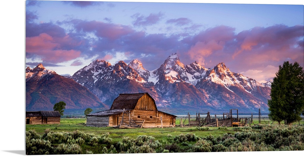 Large, horizontal photograph of an open field with an old, wooden barn and a small building next to that.  Large, snow cap...