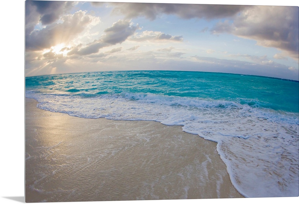 From the National Geographic Collection a wide angle photograph of the sun setting behind clouds while waves washed up aga...