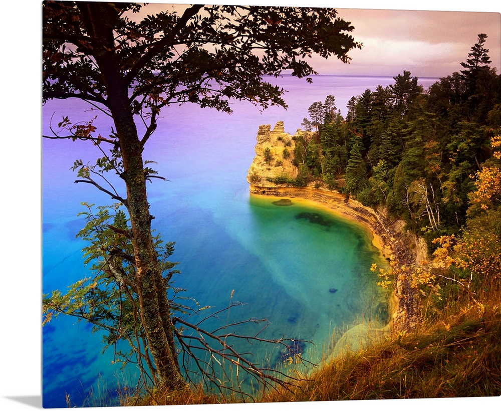 An immense cliff is covered with various trees and thick foliage that curves and overlooks Lake Superior.