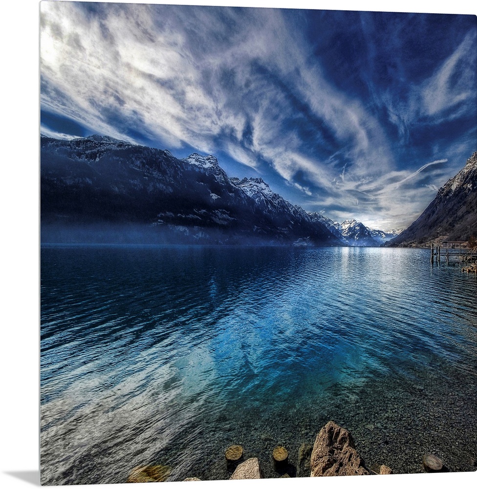 This square shaped decorative wall art is a landscape photograph of a lake surrounded by snow covered mountains beneath a ...