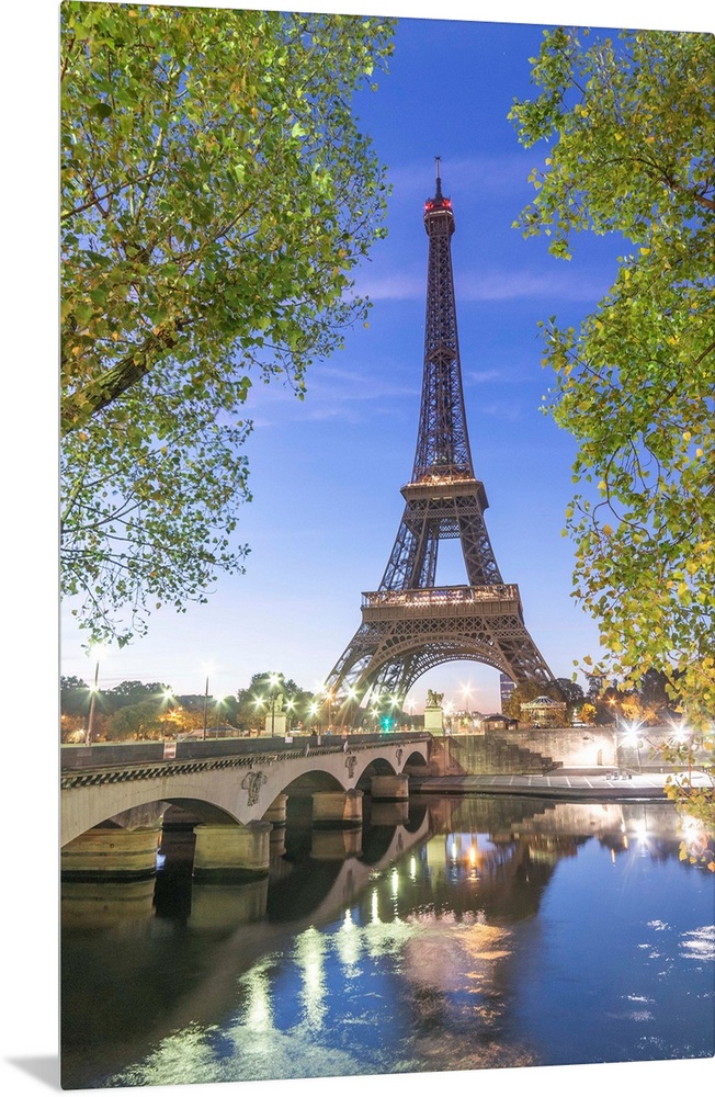 Early morning for the Eiffel tower in Paris, facing the Jena bridge with green trees around and lights.