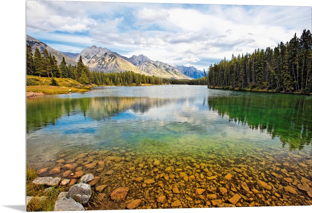 Giant photograph taken from the rocky shores of a lake that is surrounded by dense forests and snow covered mountains in t...