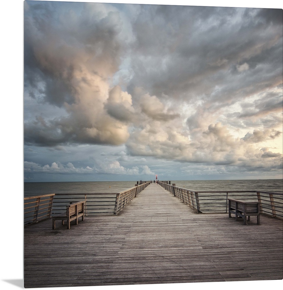 A wooden pier leading to the ocean with dramatic clouds above.