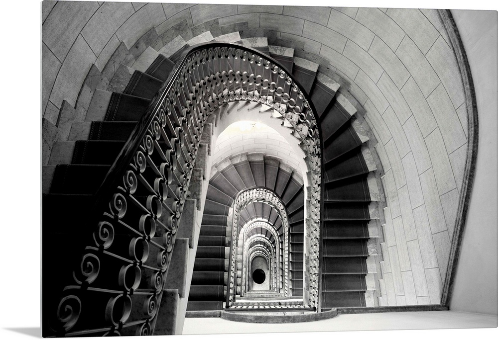 This architectural photograph looks down a historic stairwell lined with tile and iron work banister.