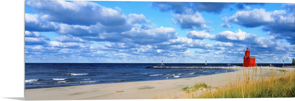 Panoramic photograph of a large lighthouse next to a dock on a sandy beach in Holland, Michigan during a sunny day.  The w...