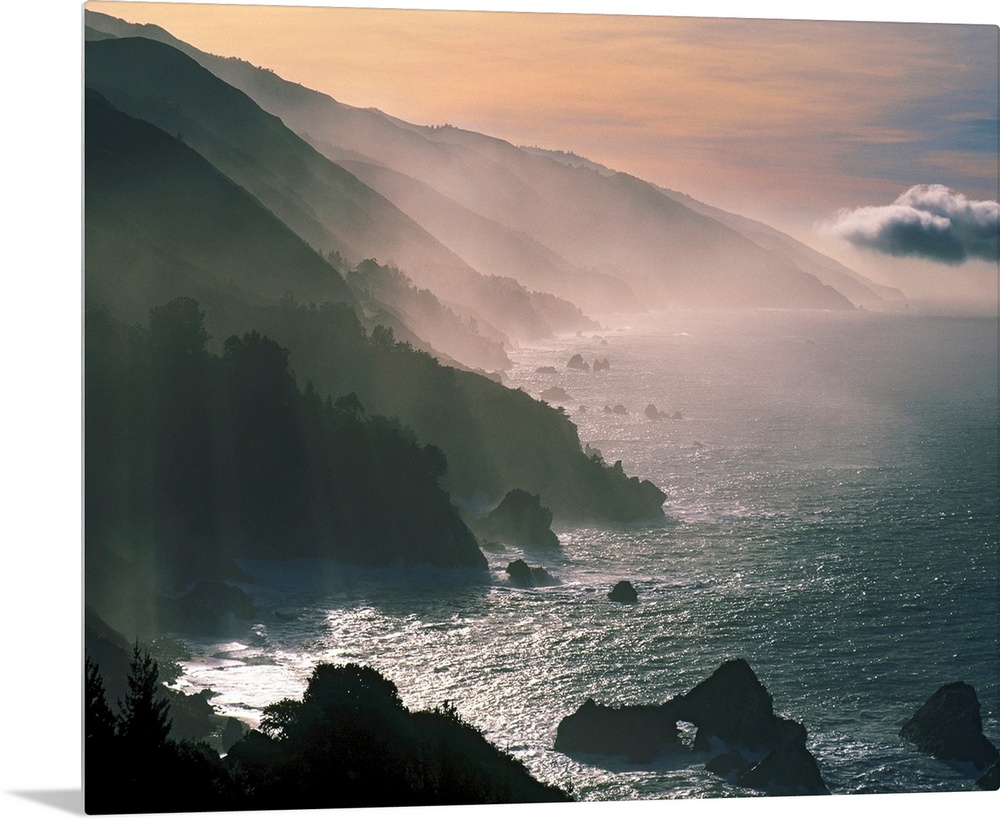 Photograph of the Santa Lucia Mountains rising through fog and mist from the Pacific Ocean.  The sky is warm with clouds i...