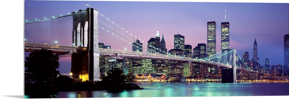 Large panoramic view of the Brooklyn Bridge lit up at night.  The waters of the East River reflecting the Manhattan skylin...