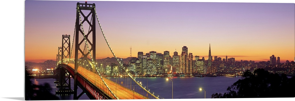Twilight and the Golden Gate Bridge with the San Francisco Skyline with a purple and gold sky.