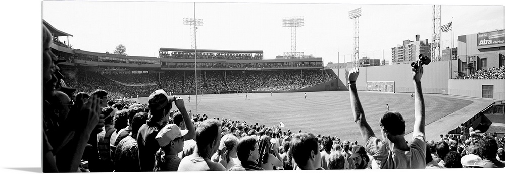 Big, panoramic black and white photograph of Fenway Park in Boston, with fans standing and cheering in the foreground.