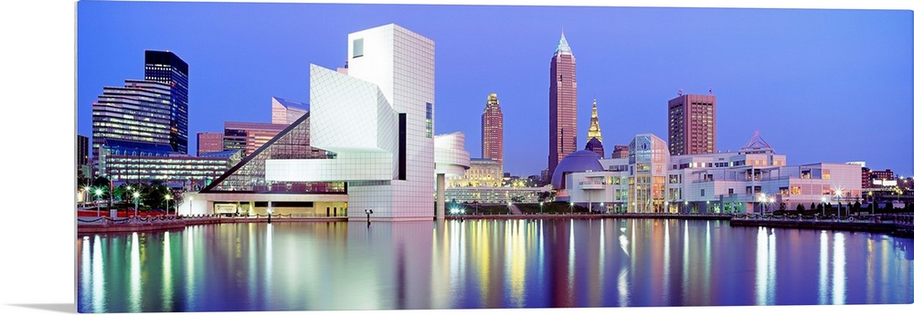 Large, panoramic photograph of the Cleveland skyline at dusk, reflecting in the waters of Lake Erie.