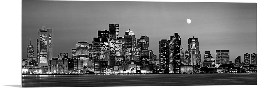 A panoramic of the skyscrapers in Boston lit up at night and the moon above the city.