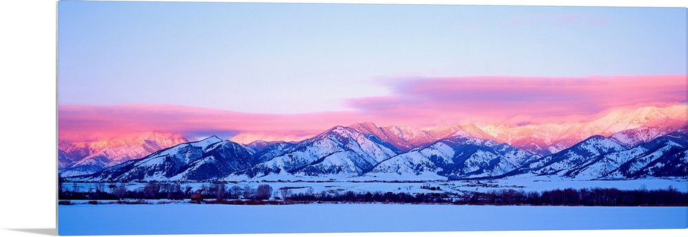 A panoramic snowscape photograph of plains and clouds passing over mountains at the end of the day.