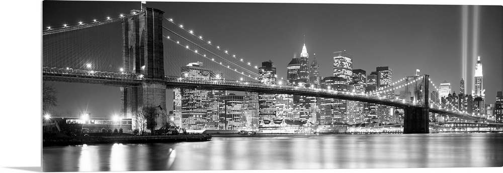 A panoramic landscape photo taken after 2001 of Manhattan and Brooklyn Bridge shining bright over the East River at night.
