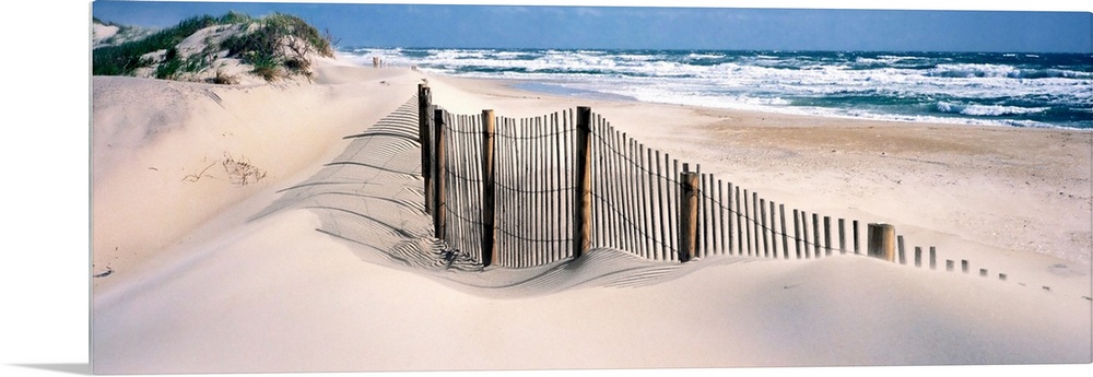 A wooden fence separates sand dunes from the Atlantic Ocean in this panoramic image.