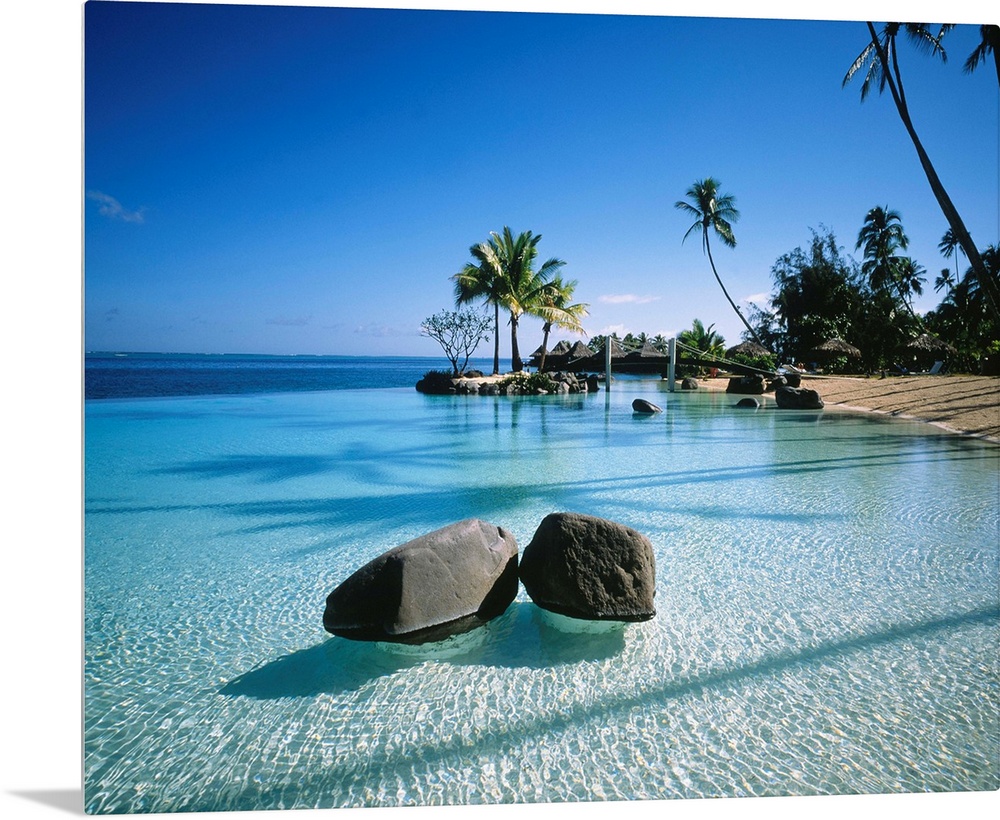 Large landscape artwork for a living room or office of clear water ripples around rocks on a tropical beach lined by palm ...