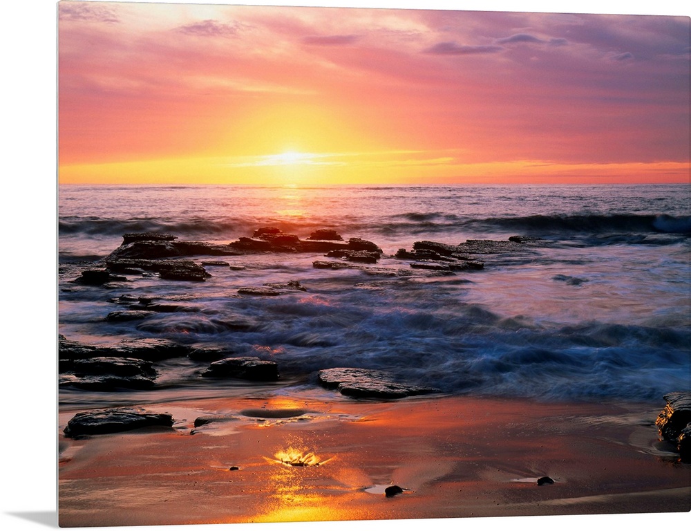 Photograph of rocky shoreline at sunset with a cloudy sky.