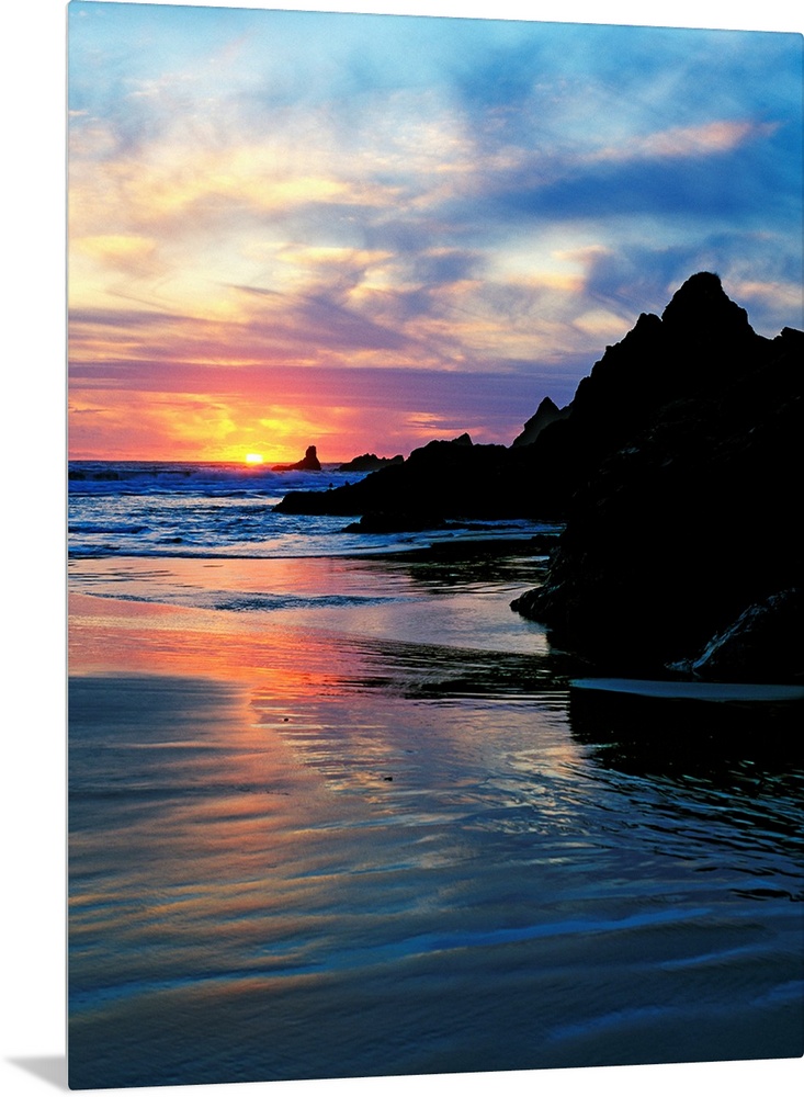 Sun below the horizon in a seascape with a rocky beach and waves.