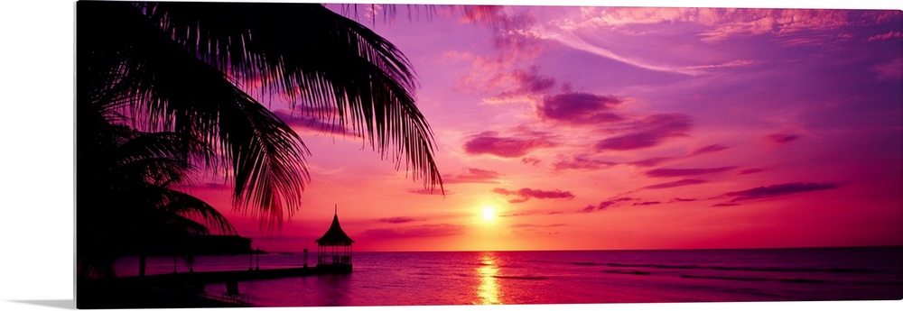 Panoramic photograph of a colorful sunset on the beach in Montego Bay, Jamaica.  The palm trees and dock in the foreground...