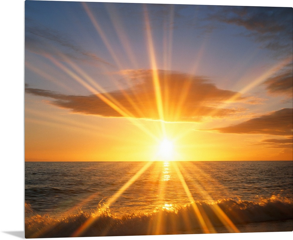 Giant photograph of a bright sunset reflecting onto an ocean as the waves crash against a sandy beach.