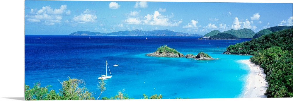 Panoramic photograph of a couple boats sitting in the clear waters of Trunk Bay in the Virgin Islands.  The mountains in t...