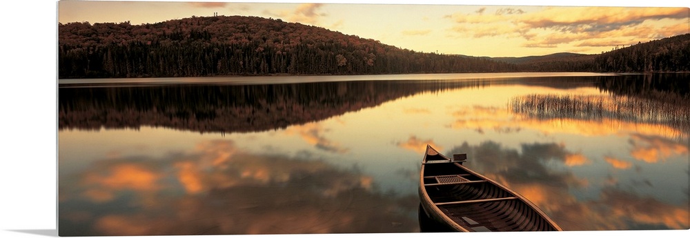 A canoe floats in a still lake at sunset in New England as clouds reflect in the water.