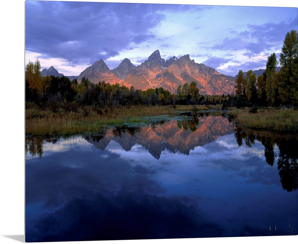 Huge photograph displays a set of jagged mountains in the background as they reflect over the calm water in the foreground...