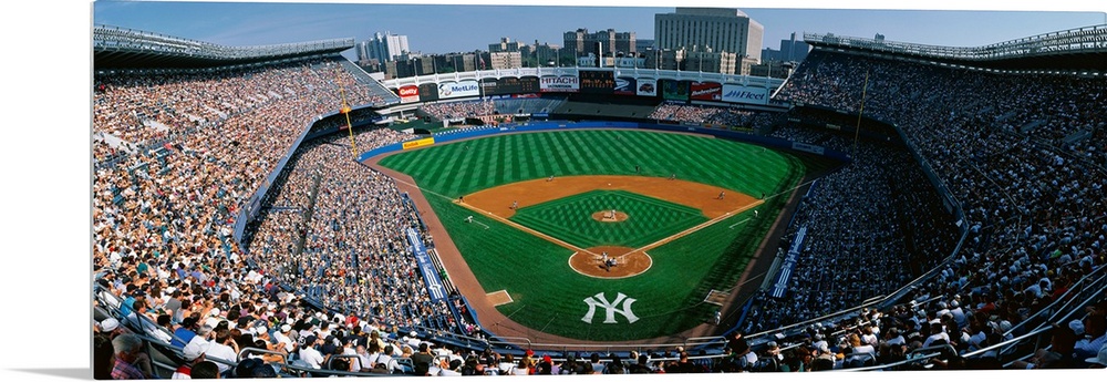 Panoramic photograph taken at Yankee Stadium in the Bronx, New York displays fans enjoying a baseball game on a sunny day....