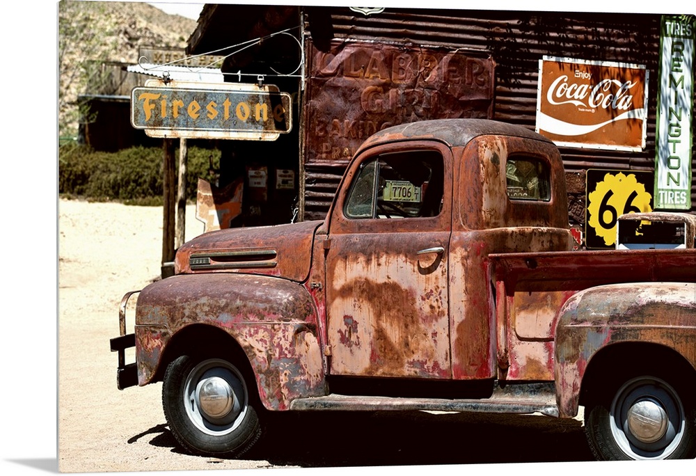 A very rusty pickup truck sits by a weathered gas station on Route 66.