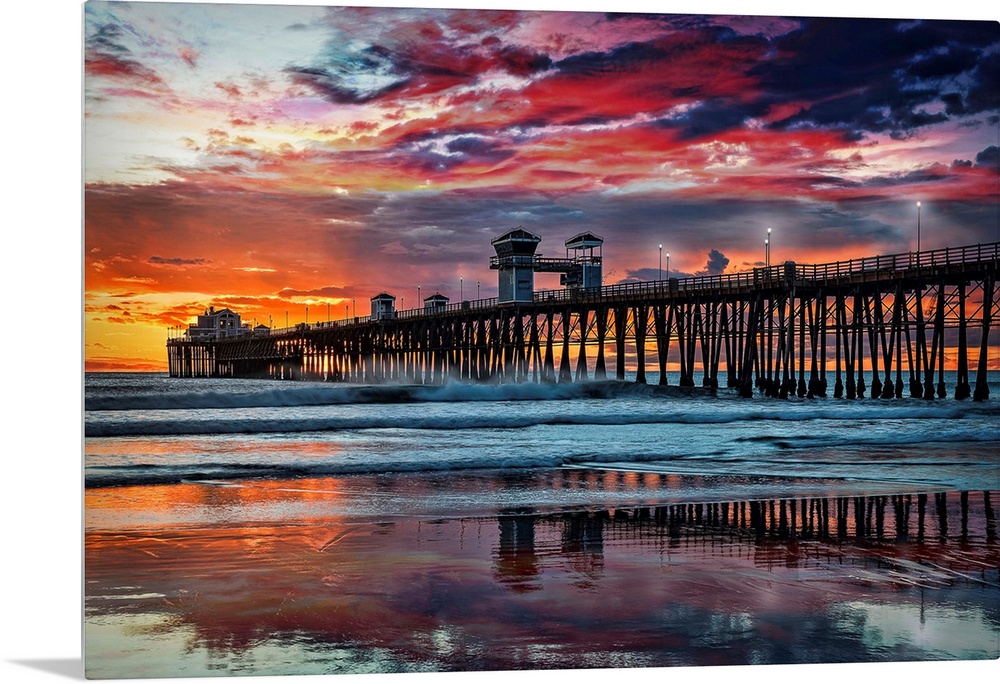 The Oceanside Pier is silhouetted as sunset turns the reflected clouds from yellow to pink to gun metal grey, and finally ...