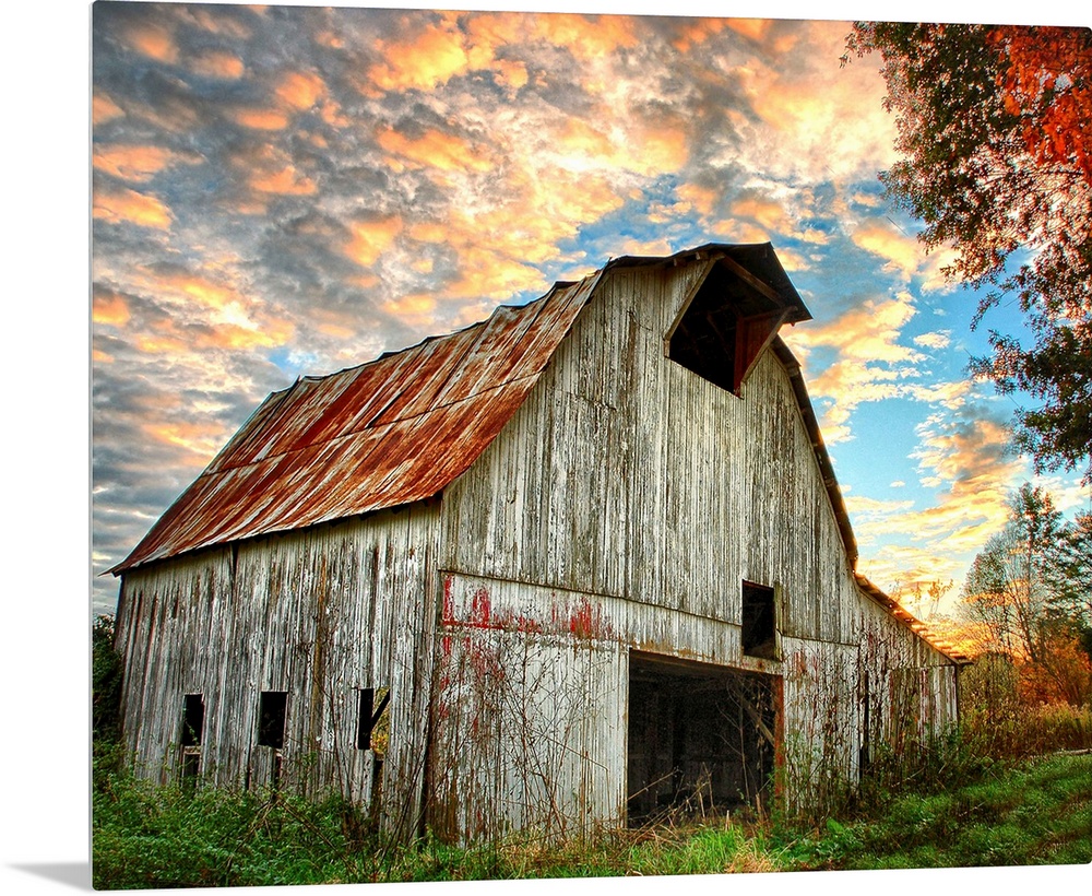 Sunset over an old, weathered barn, with a cloudy sky.