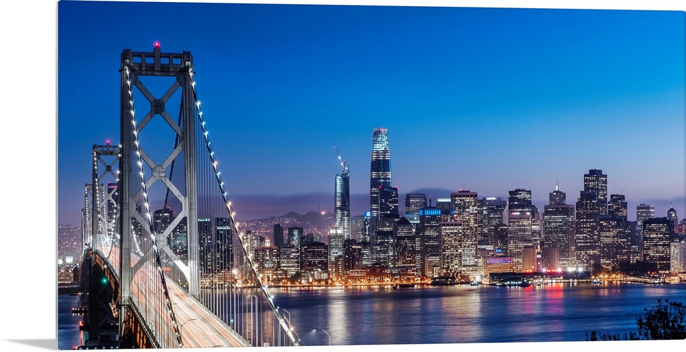 Photograph of the Bay Bridge and the San Francisco skyline lit up at dusk.