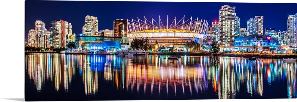 Panoramic photograph of BC Place Stadium and part of the Vancouver skyline lit up at night and reflecting onto the water, ...