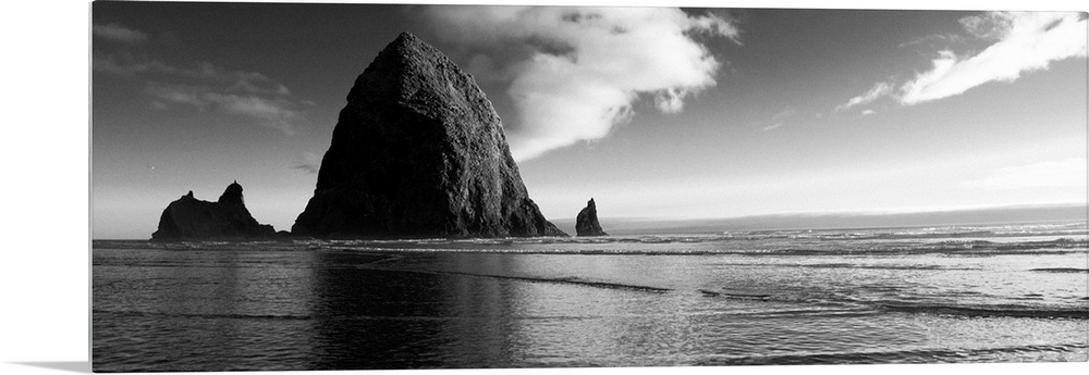 Black and white panoramic photograph of Haystack Rock with rippling waters.