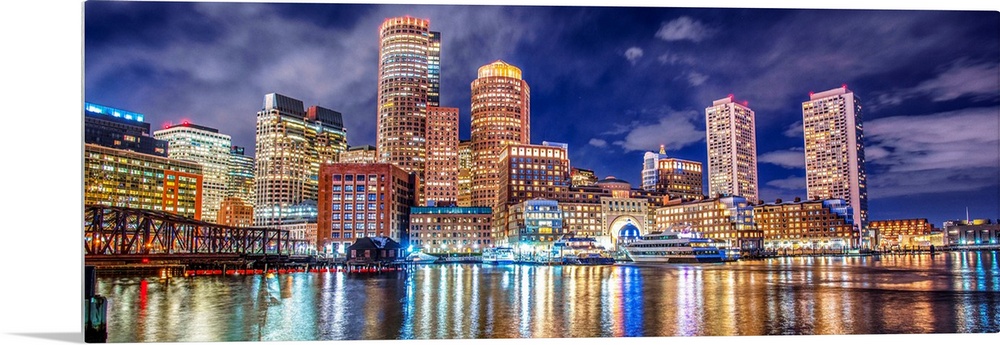 Panoramic view of the Boston City skyline at night, with lights reflected in the water.