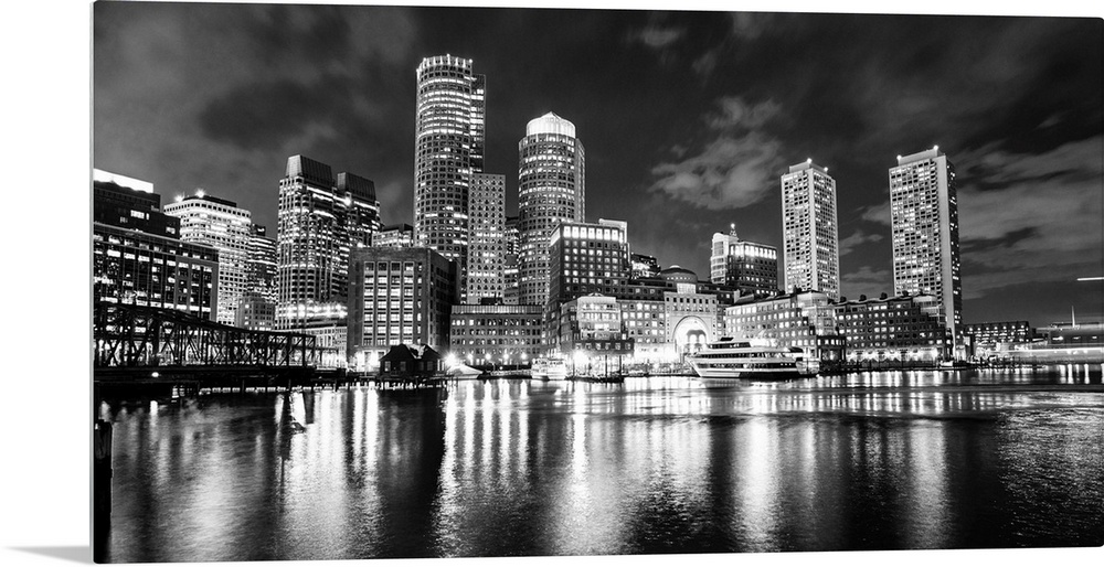 Panoramic view of the Boston City skyline at night, with lights reflected in the water.