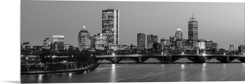 Panoramic view of the Boston City skyline illuminated at night, with the Longfellow Bridge in the foreground.