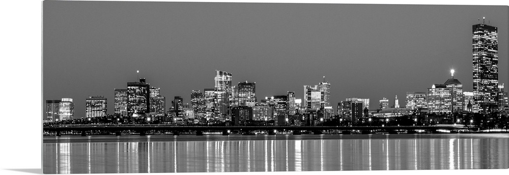 Panoramic view of the Boston City skyline at night, with lights reflected in the water.