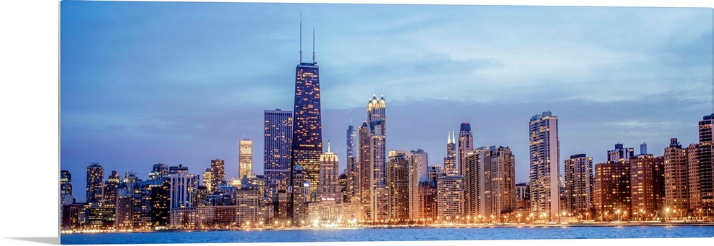 Panoramic view of the Chicago city skyline illuminated in the early evening, seen from the edge of Lake Michigan.