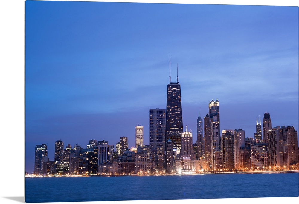 The Chicago city skyline illuminated in the early evening, seen from across the water.