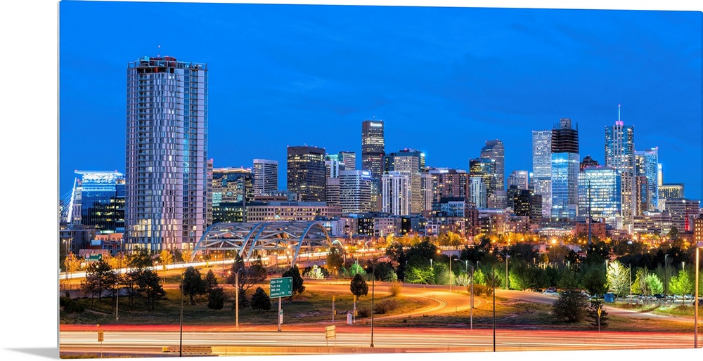 Photograph of the Denver, CO skyline at dusk with warm light trails on the highway from passing cars.