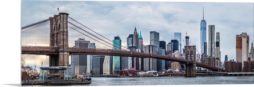 View of the New York City skyline under an overcast sky, with the Brooklyn Bridge, from across the water.