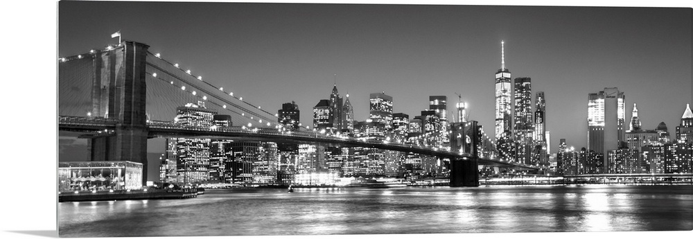 View of the New York City skyline illuminated at night, with the Brooklyn Bridge, from across the water.