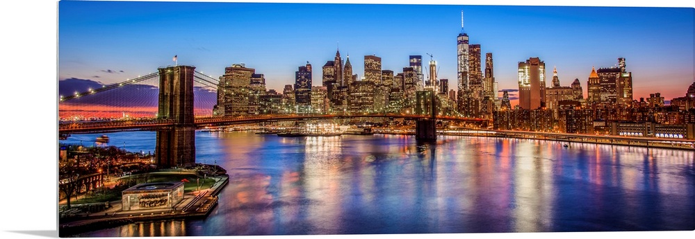 View of the New York City skyline illuminated at night, with the Brooklyn Bridge, from across the water.