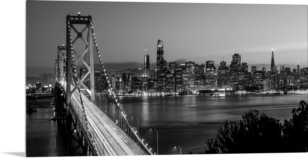 Photograph of the Bay Bridge with a sunset and the San Francisco skyline lit up in the background.